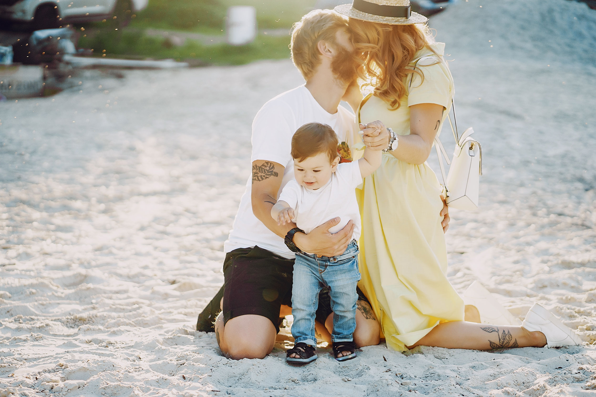 Mum and Dad kissing whilst holding baby on a beach